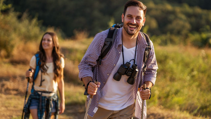 Two people hiking in a natural setting with backpacks and binoculars.